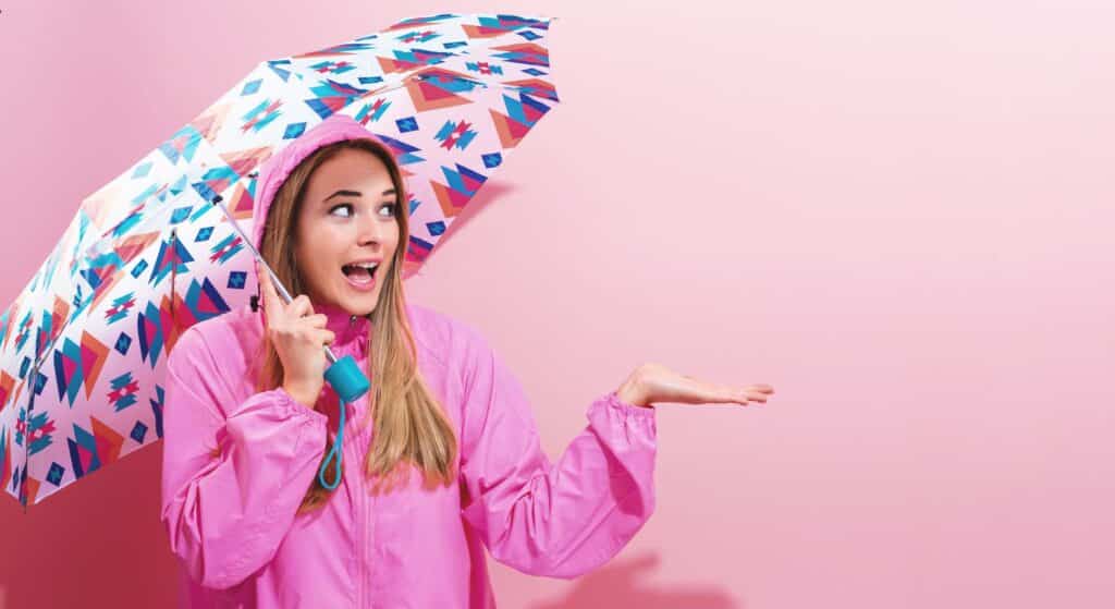 Woman in pink raincoat holding colorful umbrella against pink background