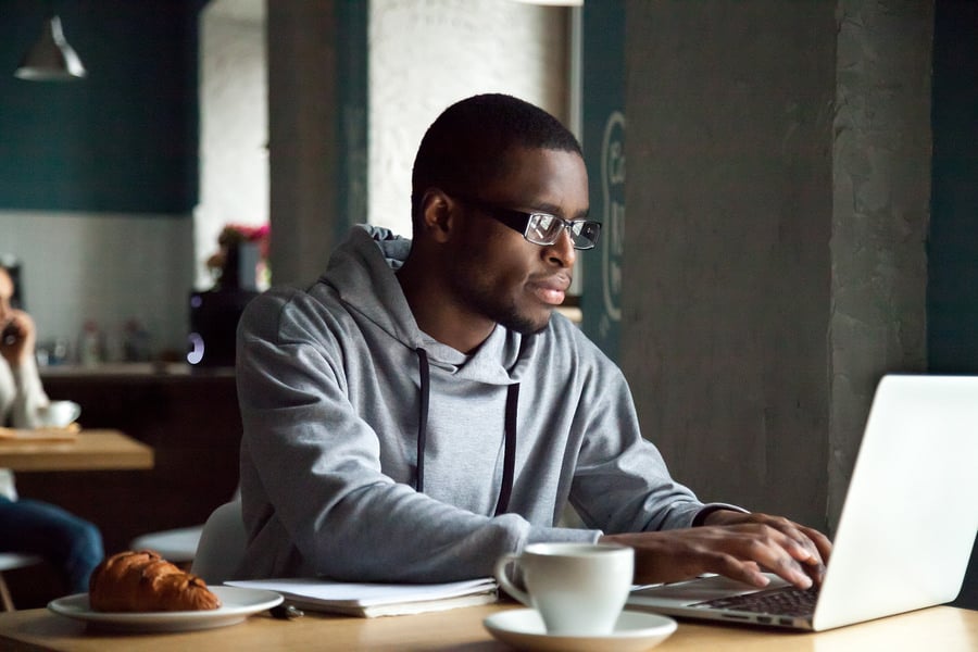 Focused African-American man using a laptop while sitting at a desk at home.