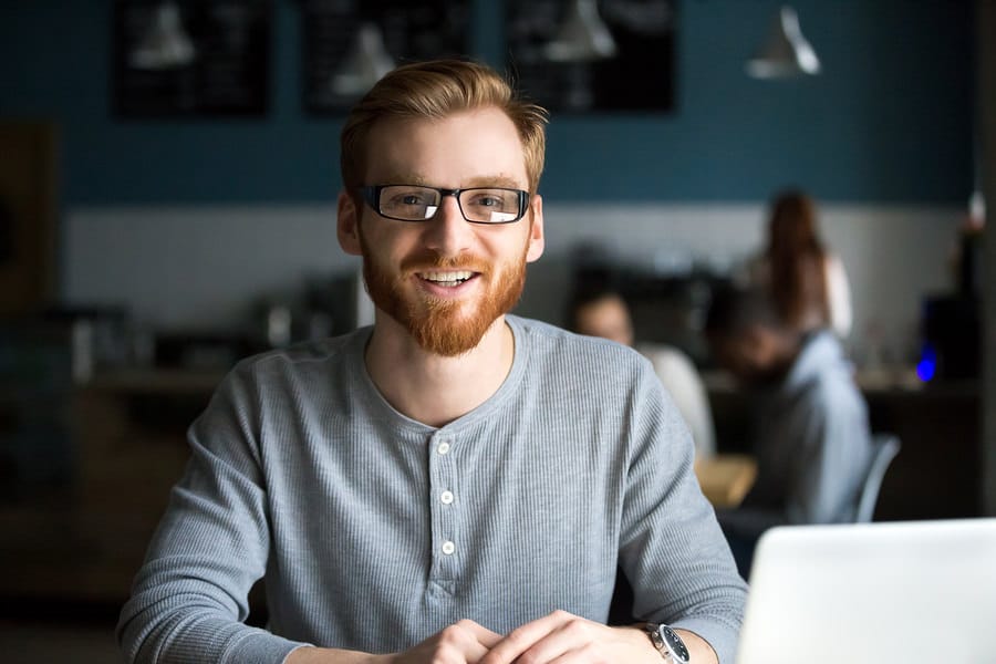 Smiling redhead man with laptop looking at camera in a cafe
