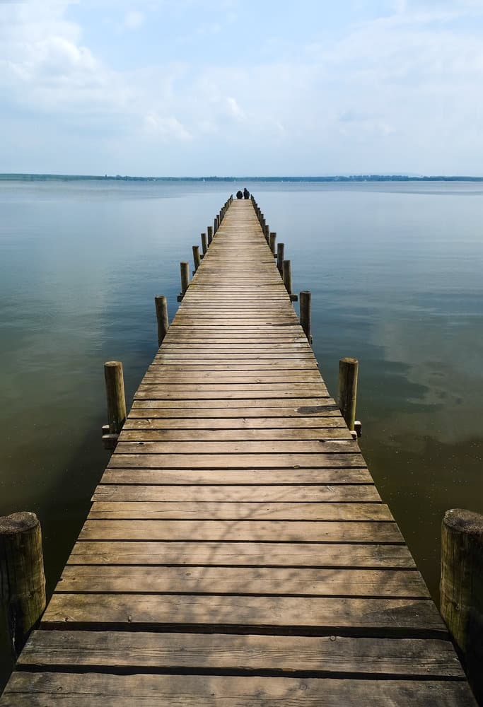 Wooden pier extending into a calm lake surrounded by fall-colored trees.