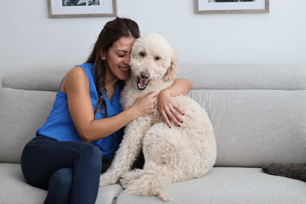 Woman smiling and hugging a fluffy white dog inside a home